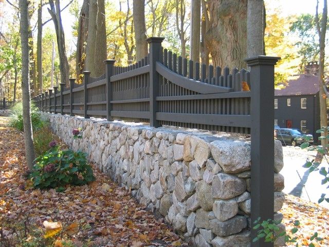 a stone wall and wooden fence in the woods