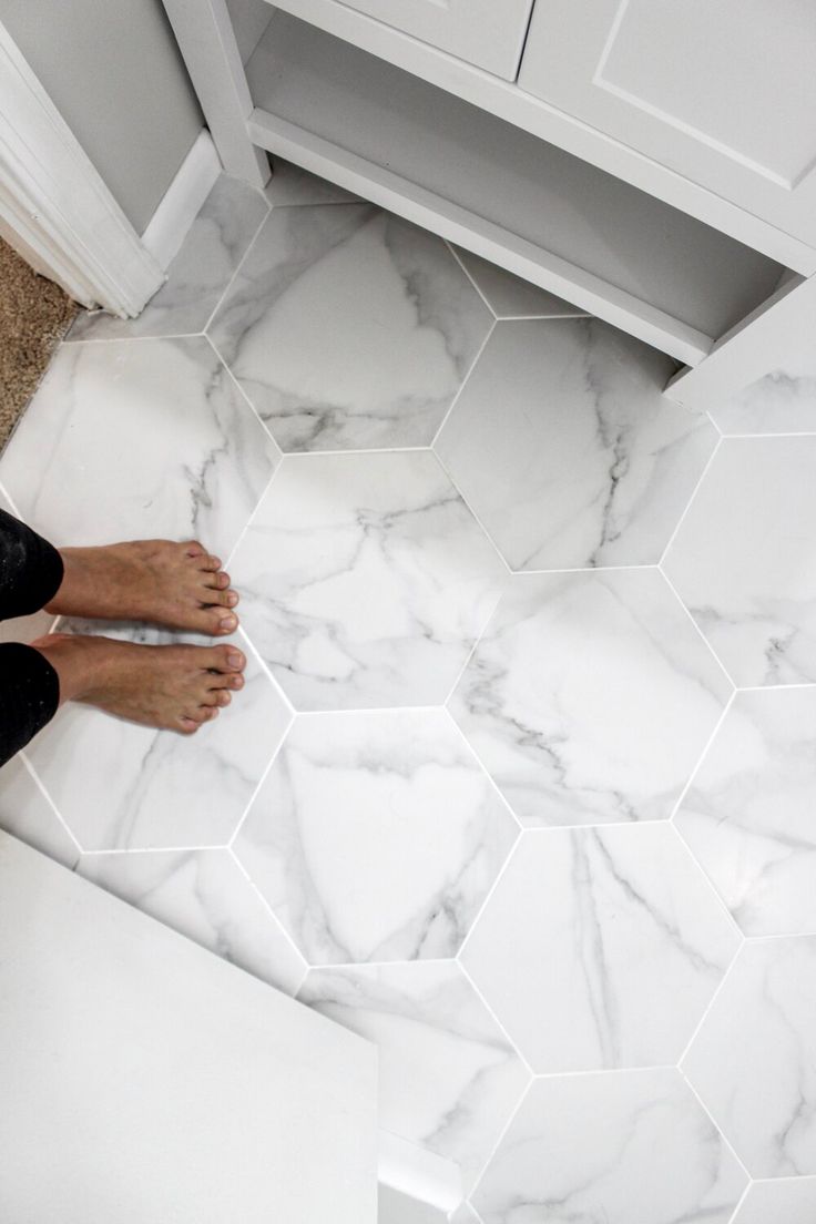 a person standing on the floor in front of a bathroom vanity with hexagonal tiles