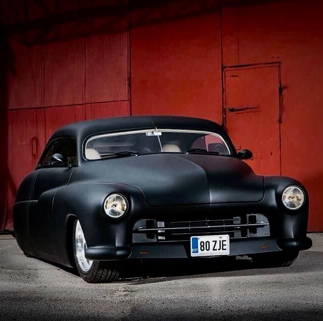 an old black car parked in front of a red building