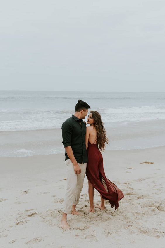 an engaged couple standing on the beach in front of the ocean