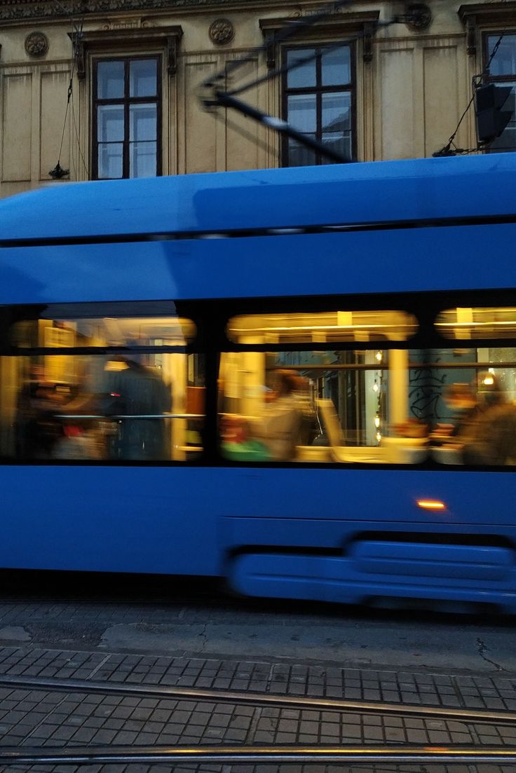 a blue bus driving down a street next to a tall building with lots of windows