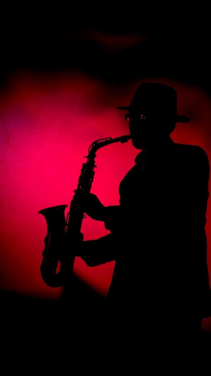 the silhouette of a man in a hat and suit playing a saxophone against a red background