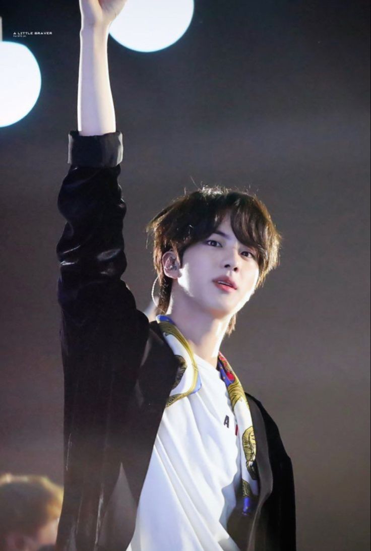 the young man is holding his hand up in the air while wearing a white shirt and black jacket