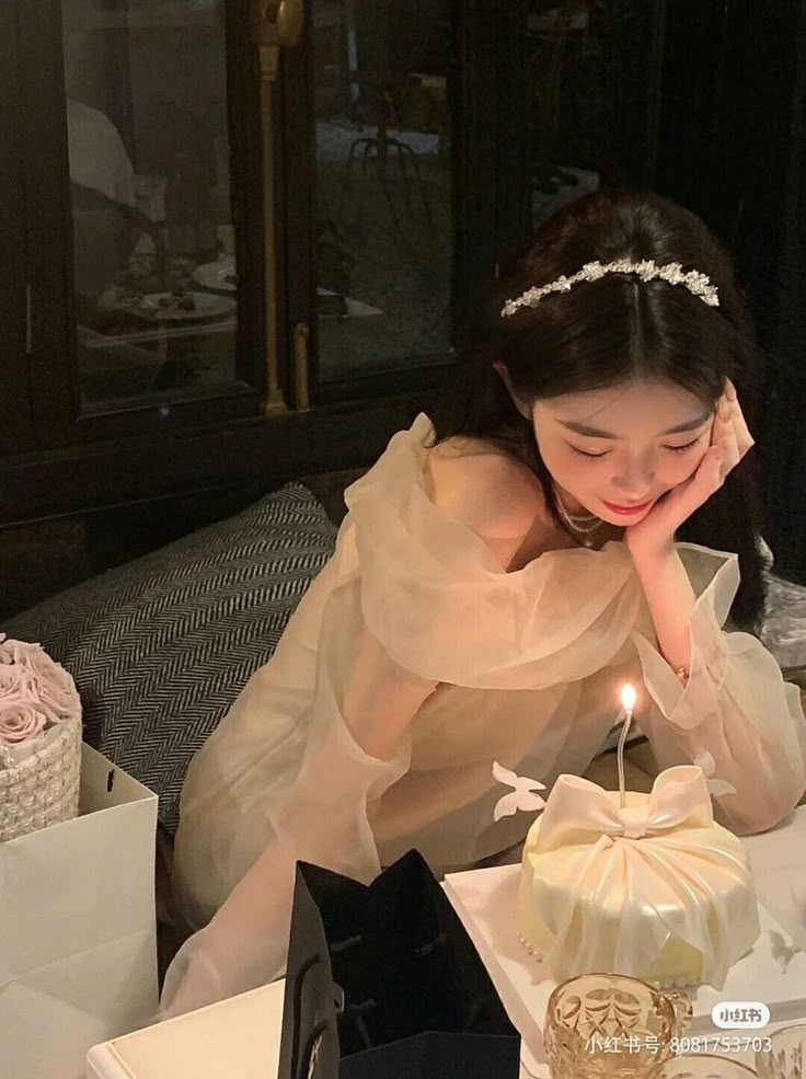 a woman sitting at a table in front of a cake with a candle on it