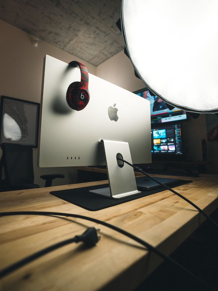 an apple computer sitting on top of a wooden desk next to headphones and a light