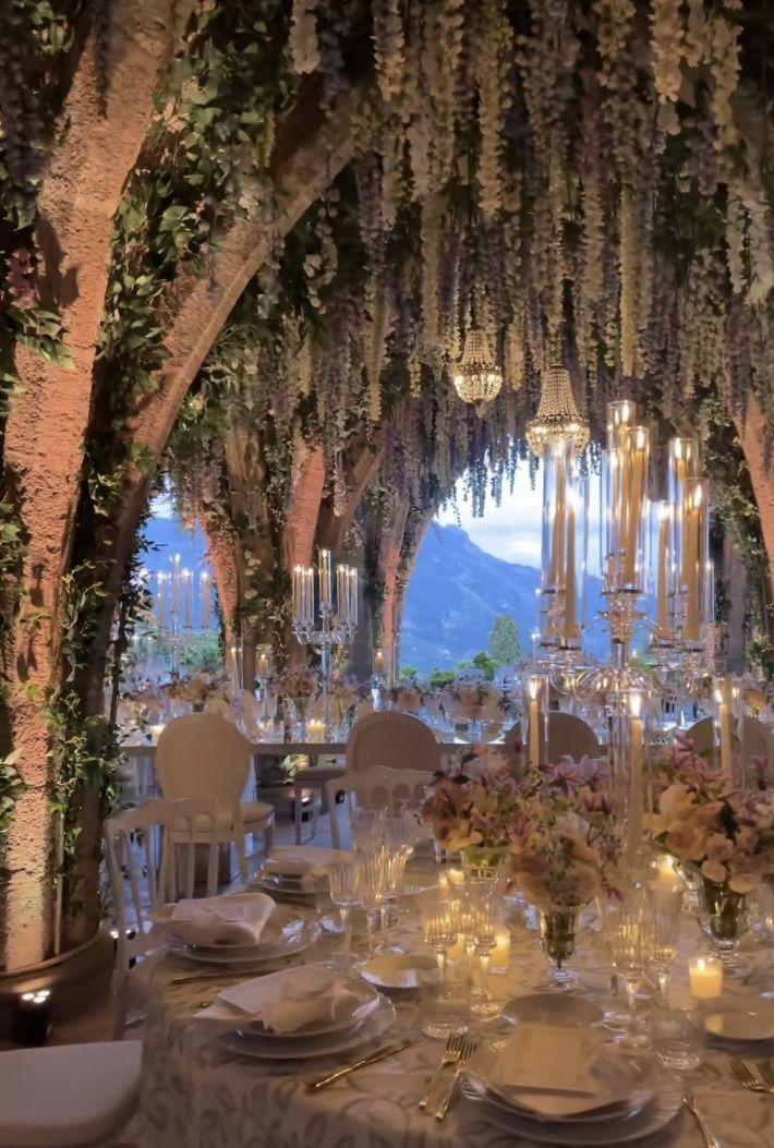 an outdoor dining area with tables, chairs and chandeliers covered in greenery