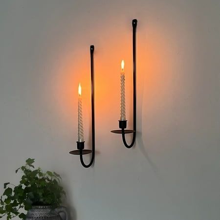 two candles are lit on the wall next to a potted plant