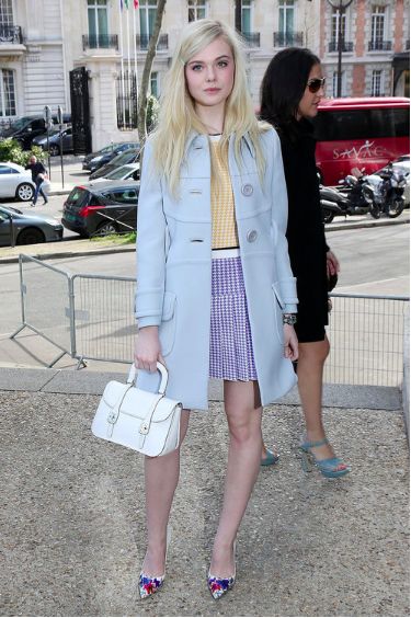 a woman in a blue coat and dress holding a white handbag while standing next to another woman