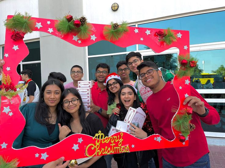 a group of people posing for a photo in front of a christmas themed frame with the words merry christmas written on it