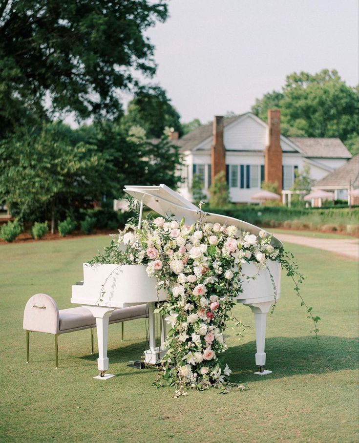 a white piano sitting on top of a lush green field next to a flower covered bench