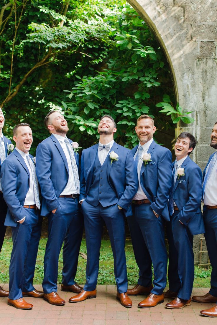 a group of men standing next to each other wearing blue suits and bow ties with trees in the background