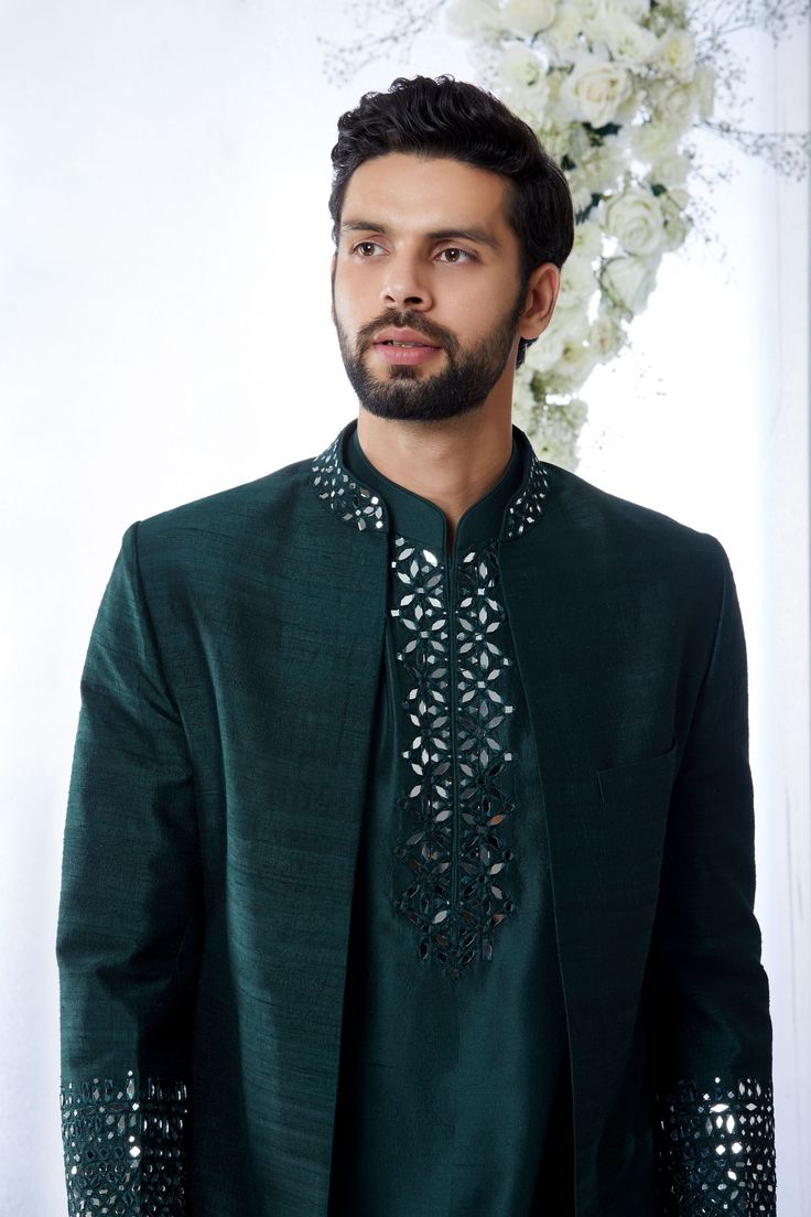 This emerald green open sherwani set features mirror work detailing on the neck and on the cuffs of the sherwani. It compliments the detailing of mirror work yoke of a silk kurta paired with a brocade trouser. Complimenting footwear is also available. From Seema Gujral's Tuscan Summer collection. DELIVERY TIMEPlease allow 8-12 weeks for your outfit to arrive.FABRIC DETAILSRaw SilkProfessional cleaning only. Emerald Green Sherwani, Mirror Work Kurta For Men, Emerald Green Mirror, Brocade Trousers, Open Sherwani, Marriage Dresses, Tuscan Summer, India Fashion Men, Jodhpuri Suits