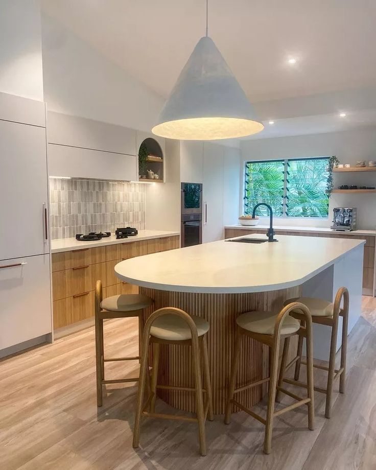 a kitchen with an island and stools in the center, surrounded by wooden flooring