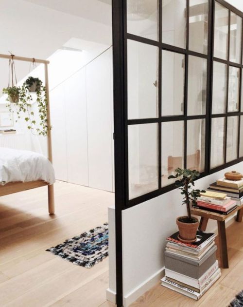 a bedroom with white walls and wooden flooring next to a bed, books on a table