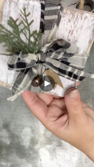 a person holding a present wrapped in plaid paper and tied with twine, on top of a table