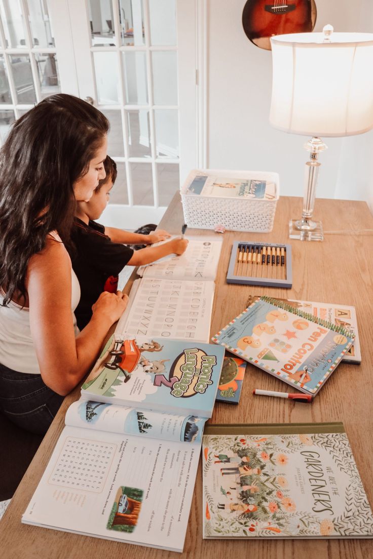 a woman sitting at a wooden table with books and crayons on the table