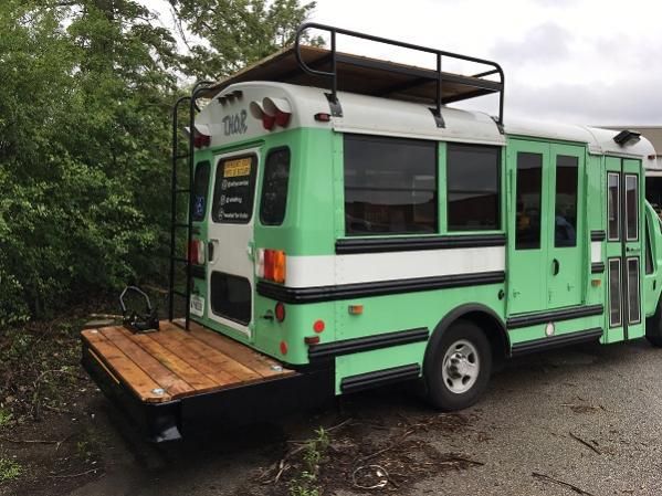 a green and white bus is parked on the side of the road near some trees