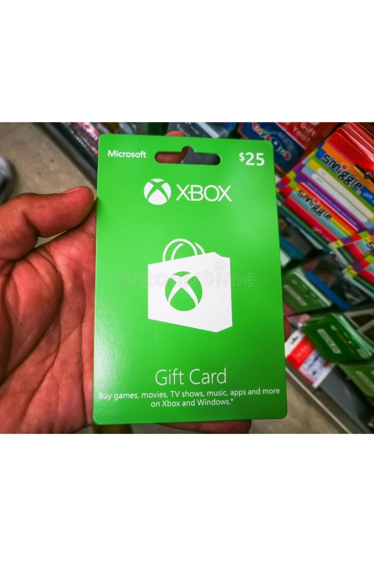 a hand holding a microsoft gift card in front of a pile of games on the shelf