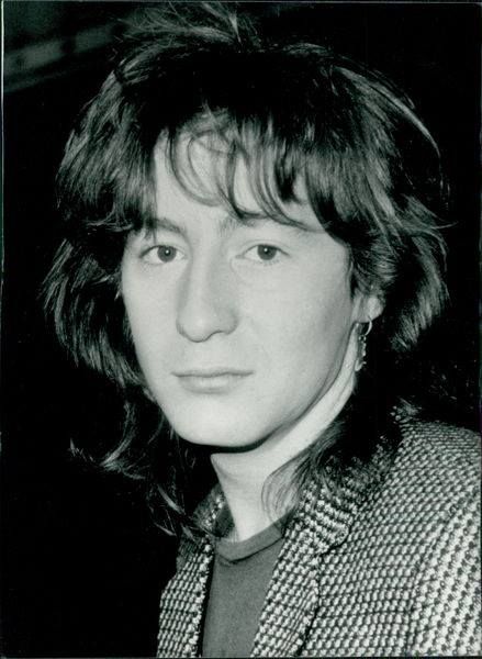 a black and white photo of a man with long hair wearing a suit jacket and tie