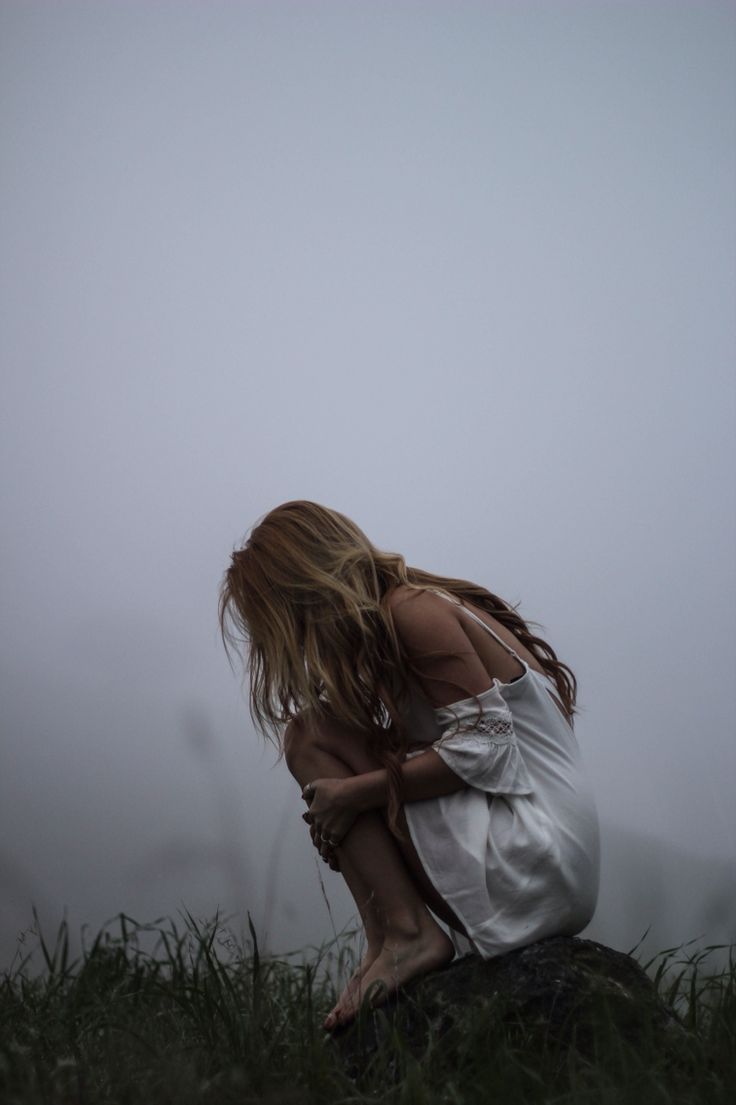 a woman sitting on top of a rock in the middle of a foggy field