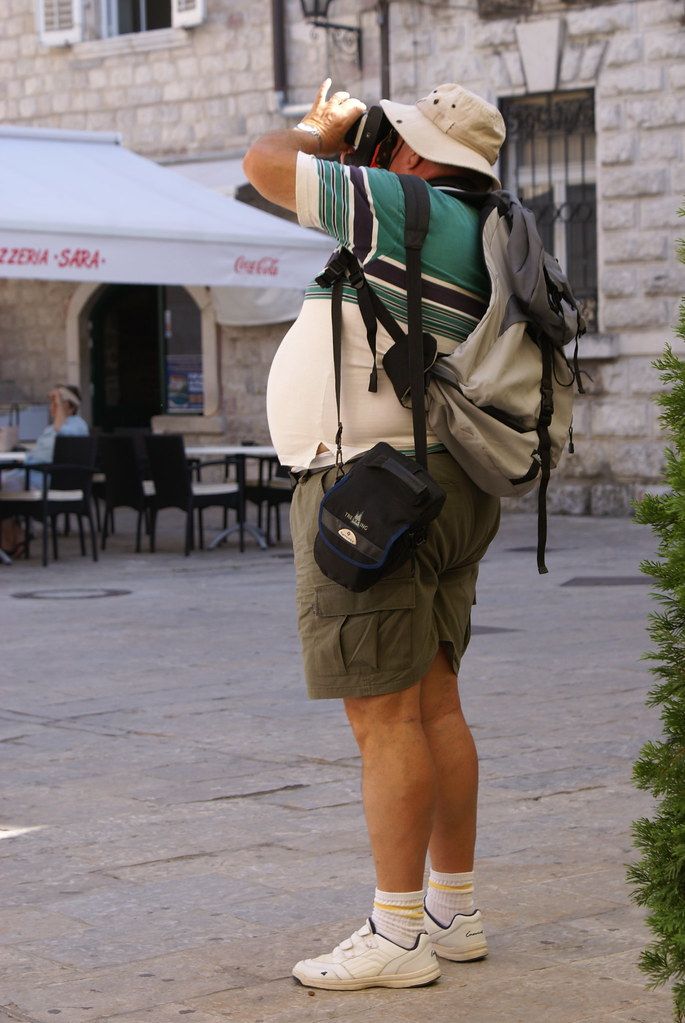 a man with a back pack is standing in front of a building drinking from a bottle