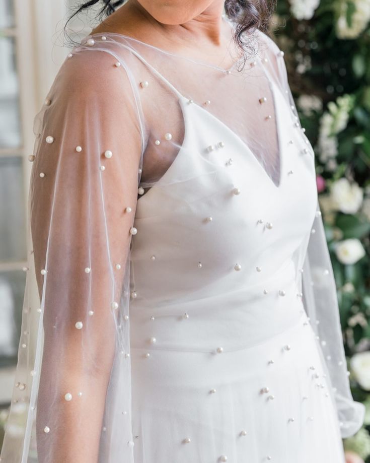 a woman in a white dress with pearls on her head and veil over her face