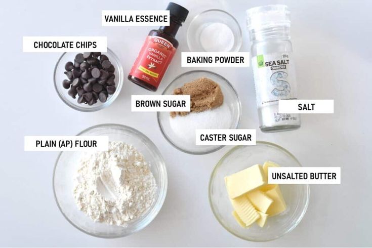 ingredients to make chocolate chip cookies laid out on a white counter top, including flour, butter, sugar, and baking powder