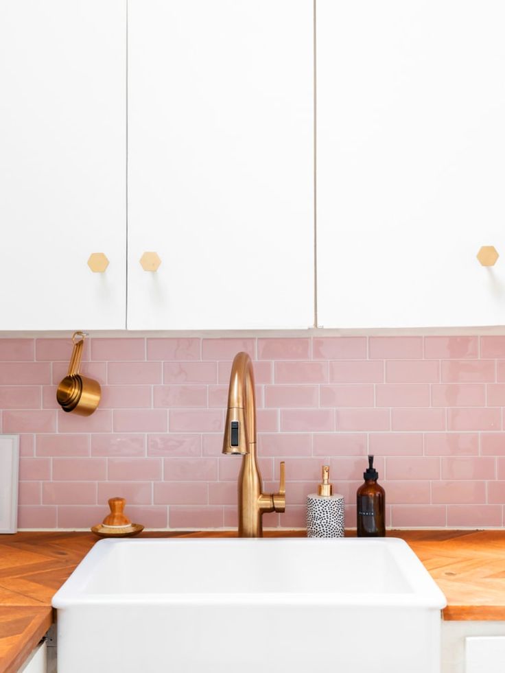 a kitchen with white cabinets and pink tiles on the backsplash, gold faucets