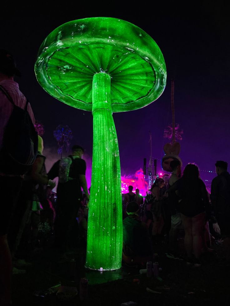 people are standing around in the dark with green lights on them and there is a large mushroom like object that appears to be lit up