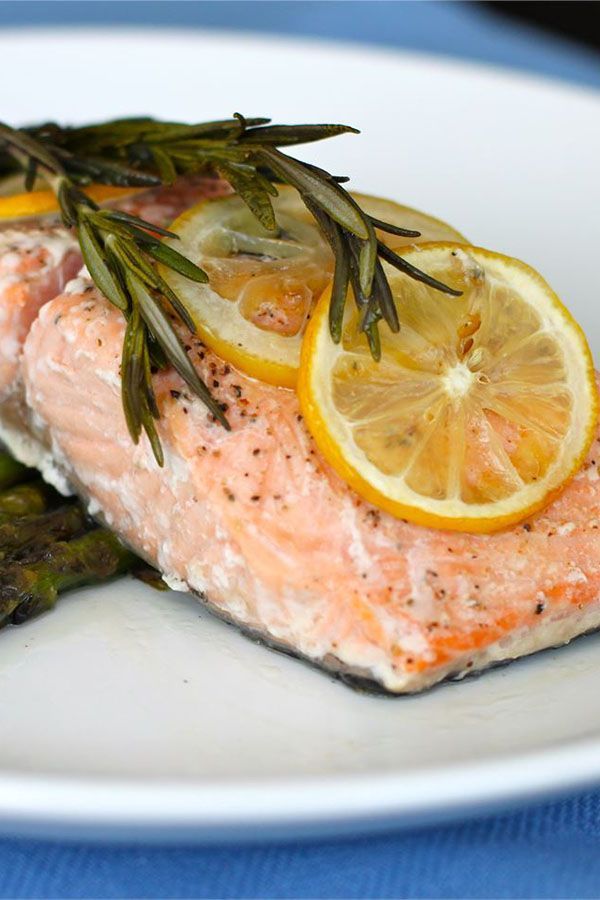 a piece of salmon on a plate with asparagus and lemons next to it