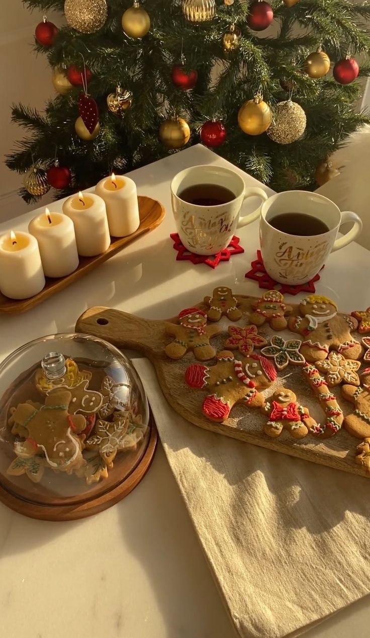 a table topped with cookies and cups of coffee next to a christmas tree filled with ornaments