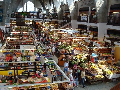 an indoor market filled with lots of food and people walking through it on either side of the aisles