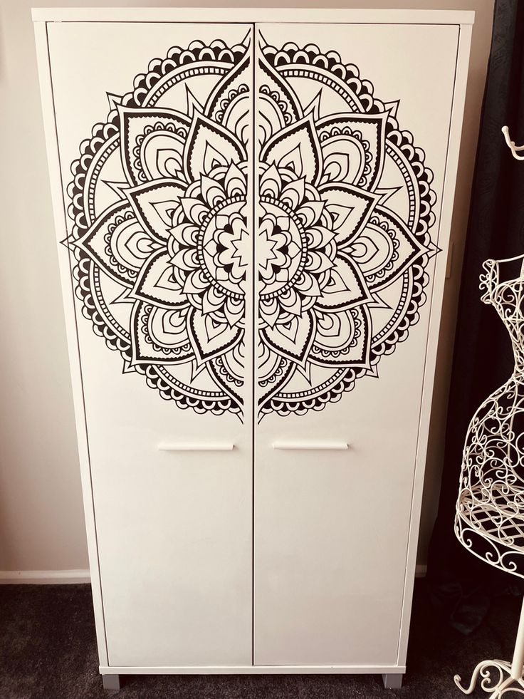 a white cabinet with an intricate design painted on the front and side doors is shown