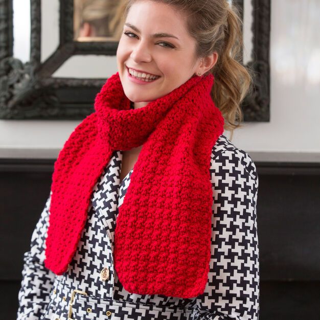 a woman wearing a red knitted scarf in front of a fireplace with a mirror behind her