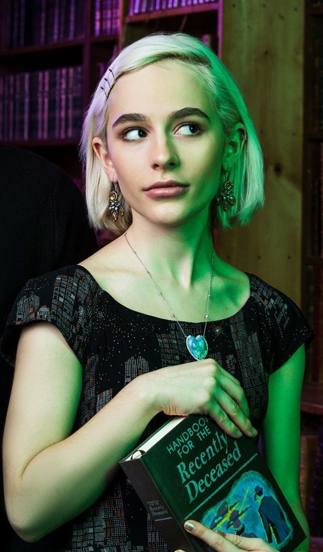 a woman holding a book in front of a bookshelf full of books and wearing earrings