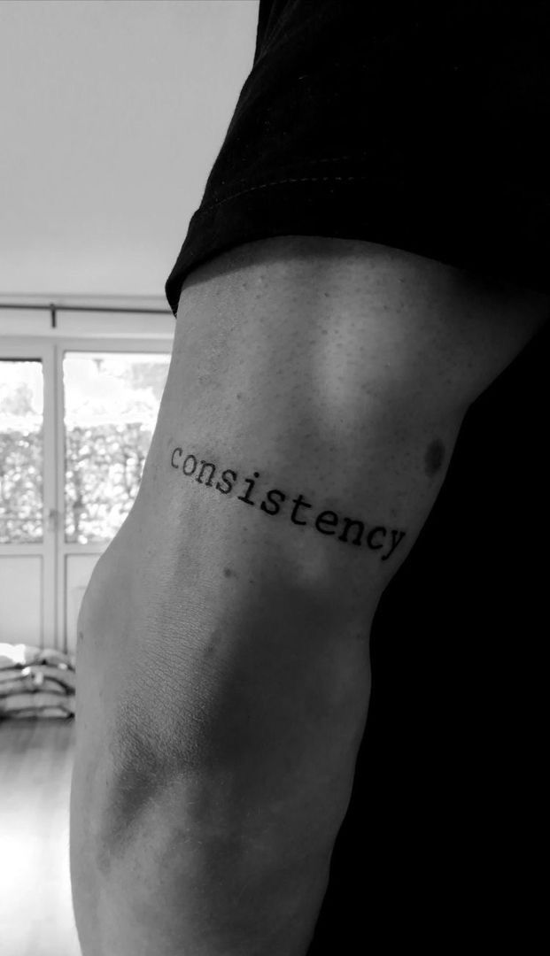 a black and white photo of a man's arm with the word constistency tattooed on it