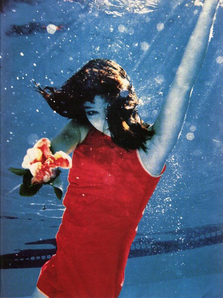 a young woman in a red dress under water holding a flower with her right hand