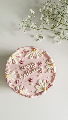 a pink cake with white flowers on it and the words happy birthday written in frosting