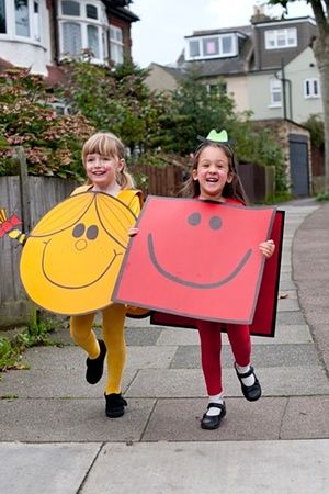 two girls in costumes holding up large pieces of paper with faces on them and smiling