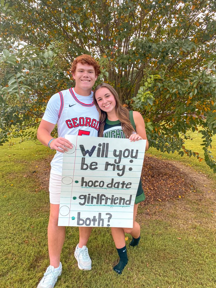 a man and woman holding a sign that says will you be my hoco date girlfriend both?