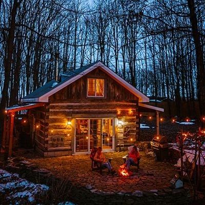 people sitting around a fire pit in front of a log cabin with lights on it