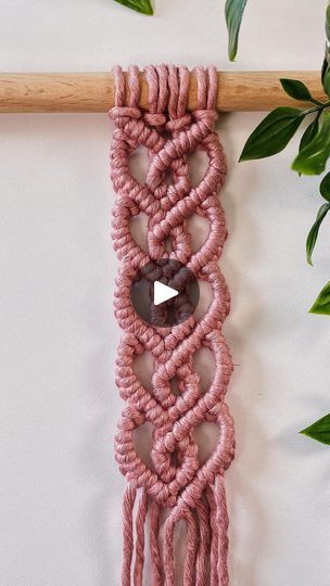 a pink macrame hanging on a wall next to a plant