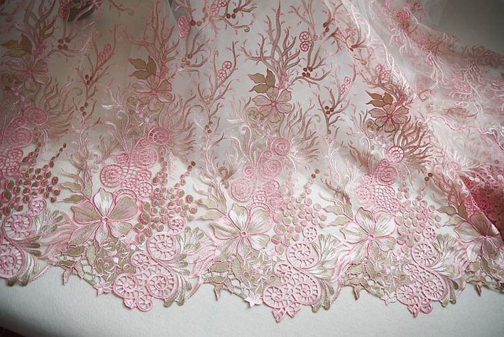 a pink and gold lace fabric with flowers on the bottom, sitting on top of a table