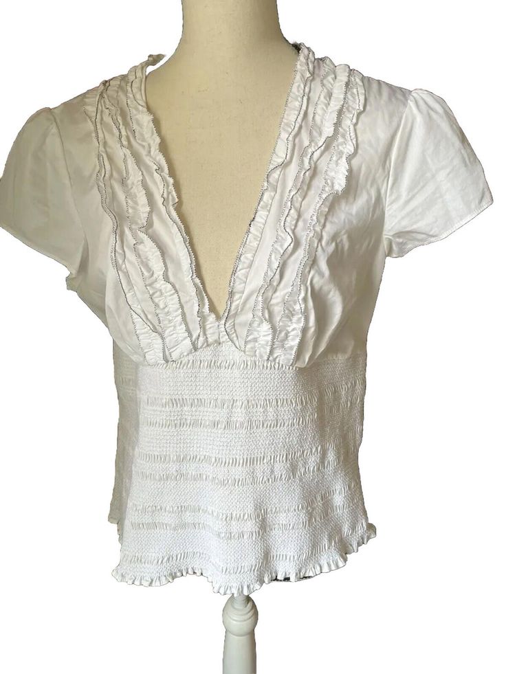 This Venus Blouse In Size 14 Features A Deep V-Neckline With Smocking And Ruffled Accents, Perfect For A Casual Occasion. The Short Flutter Sleeves And Pullover Closure Make It Easy To Wear, While The Woven Fabric With Nylon, Spandex, And Cotton Materials Provides Stretch And Comfort. The Solid White Color And Classic Fit Make It A Versatile Addition To Any Wardrobe, Suitable For All Seasons. Whether You Pair It With Jeans Or Dress It Up With A Skirt, This Blouse From Venus Is Sure To Become A F Elegant Smocked Stretch Top For Summer, V-neck Top With Smocked Back For Brunch, Elegant Smocked Top With Short Sleeves For Summer, Elegant Smocked Short Sleeve Top For Summer, Elegant Short Sleeve Smocked Top For Summer, White Tops With Smocked Back And Short Sleeves, Fitted White Blouse With Smocked Back, Fitted Smock Peasant Top For Summer, Fitted Smock Blouse For Summer