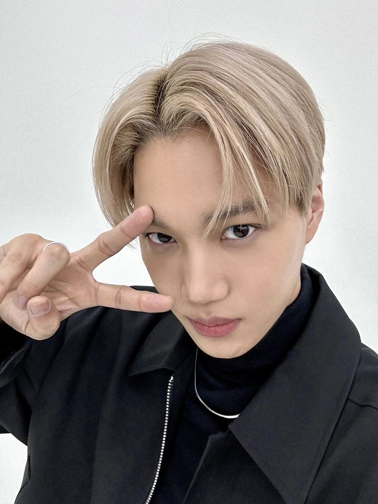 a young man with blonde hair is posing for the camera while holding his finger up to his face