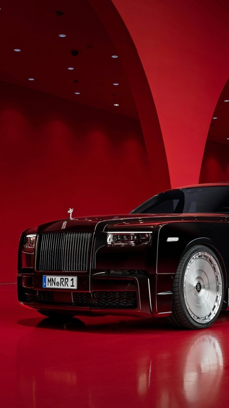 a black and red rolls royce parked in front of a red wall with white rims