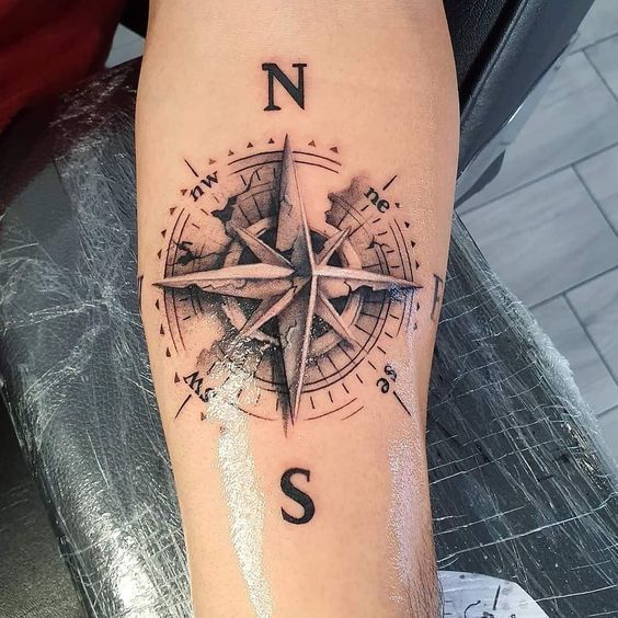 a black and white compass tattoo on the right leg, with an s in it's center