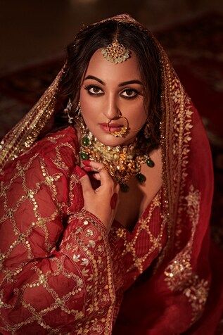 a woman in a red and gold bridal outfit posing for the camera with her hands on her chest