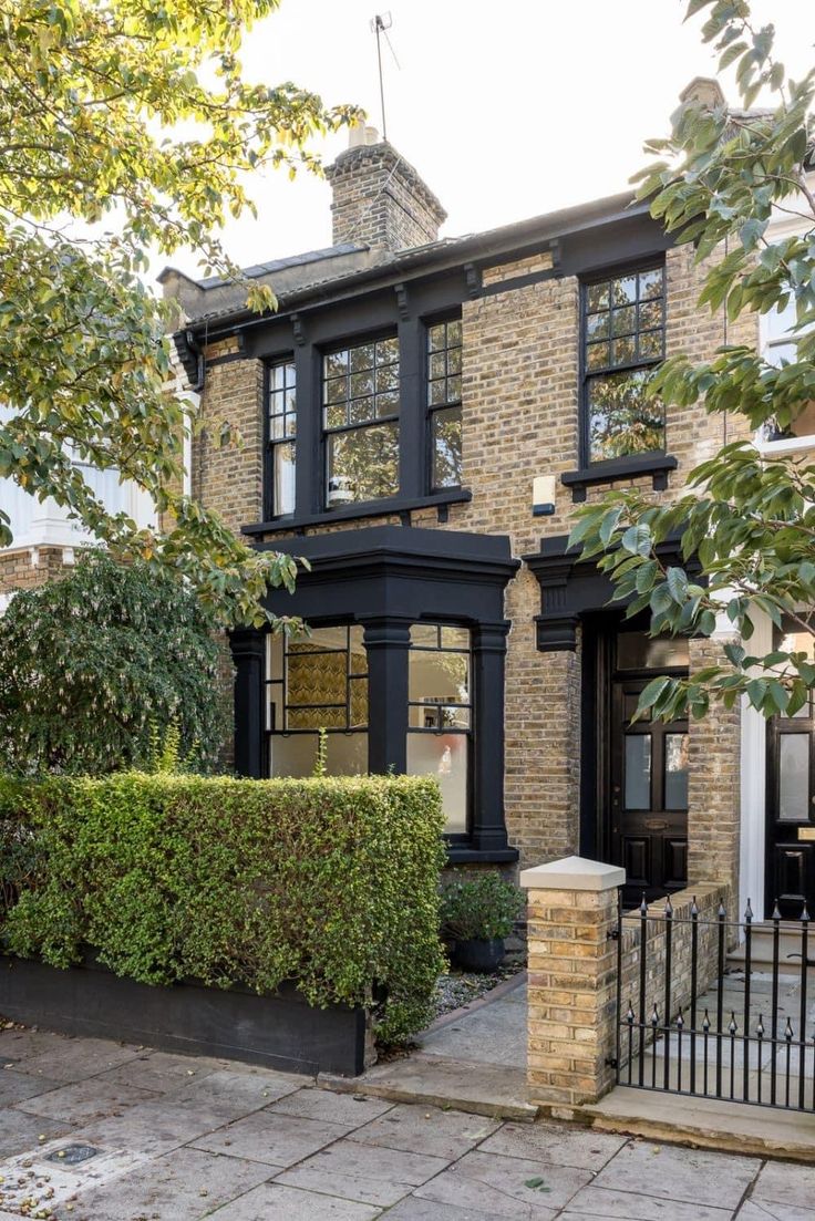 a house with black trim and windows in the front yard, surrounded by greenery