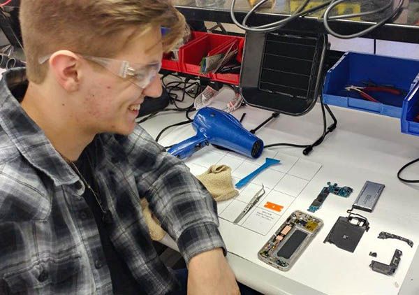 a young man sitting at a desk working on an electronic device with wires and tools around him